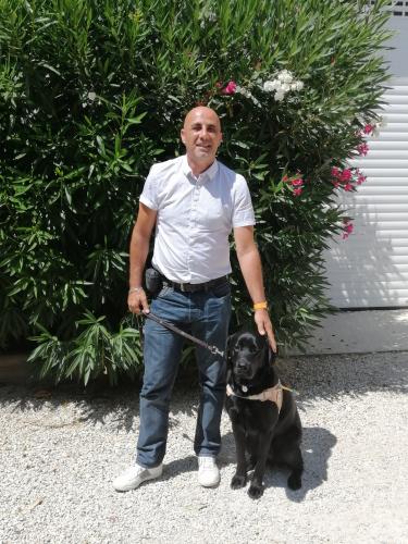 Jean-Marie se tient debout et caresse de la main gauche Pago, son chien guide, labrador noir.