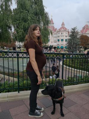Christelle est debout dans le parc Disney land et tiens son chien au harnais