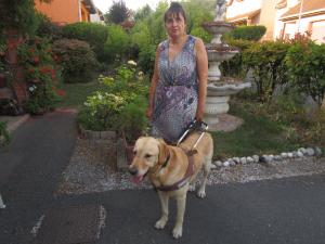 Karine, une femme brune qui tiens son chien guide, un labrador sable au harnais 