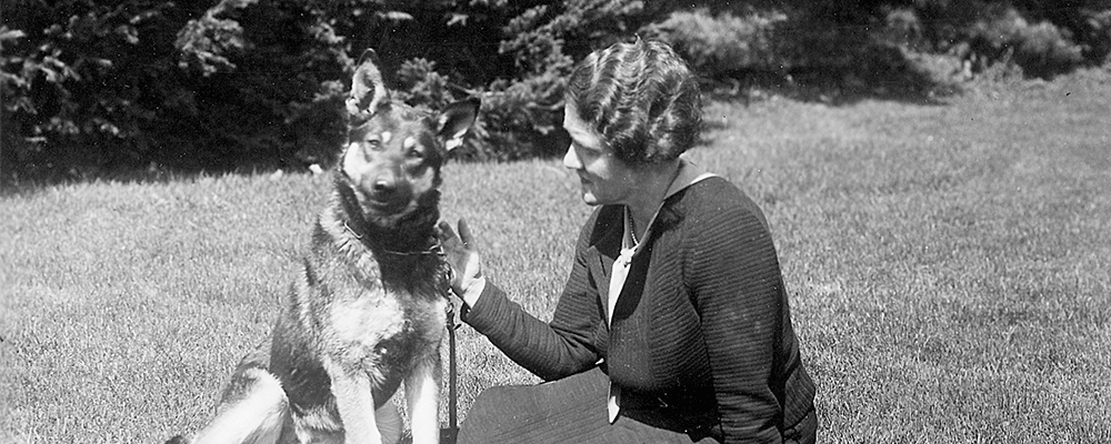 Photo de Dorothy Harrison Eustis, assise dans l'herbe avec un berger allemand.