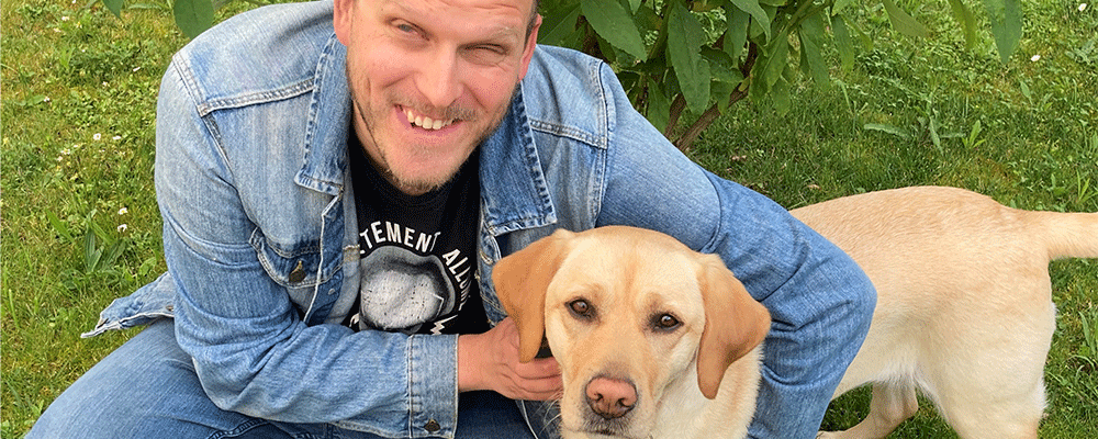 Photo de Antoine Thiebault souraitn avec son chien guide Sunny, un labrador sable.