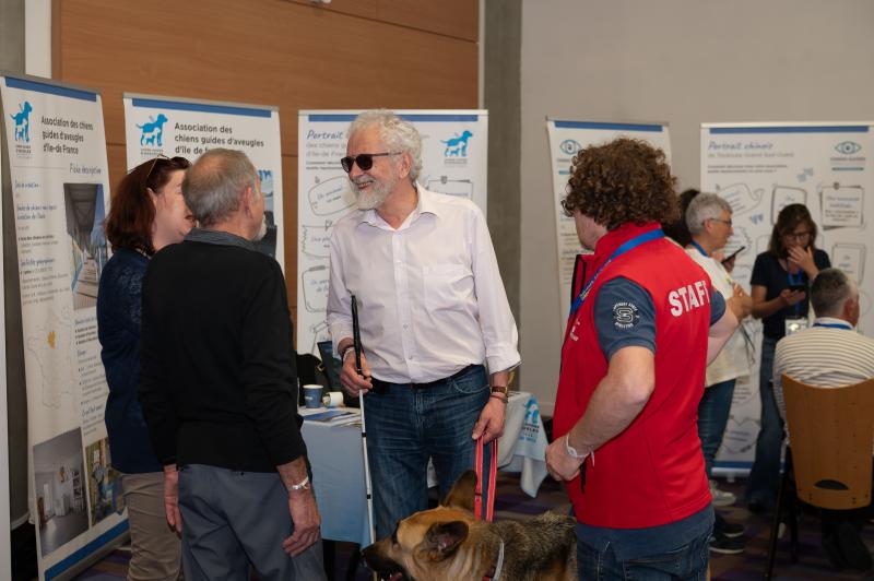 Michel Rossetti, président de la FFAC, et son chien guide visitent le village associatif du Congrès, où les associations membres présentent leurs activités et partagent leurs expériences autour du chien guide, de la déficience visuelle, du bien-être animal et de l’accompagnement des bénéficiaires.
